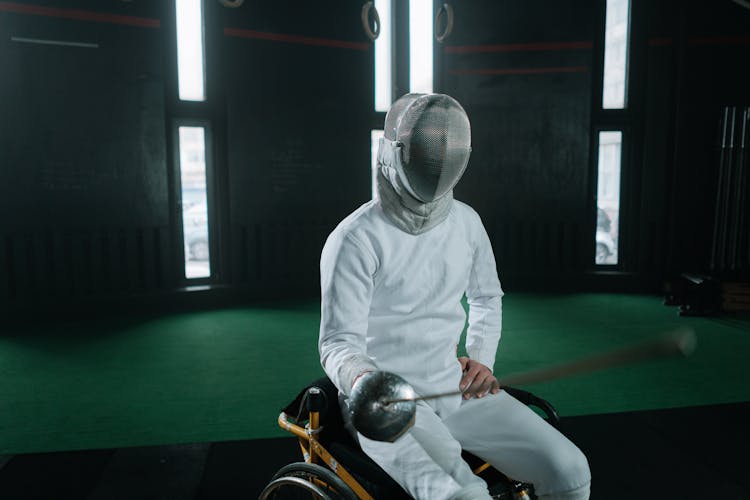 A Paralympic Athlete Sitting On A Wheelchair And Holding A Foil To The Camera