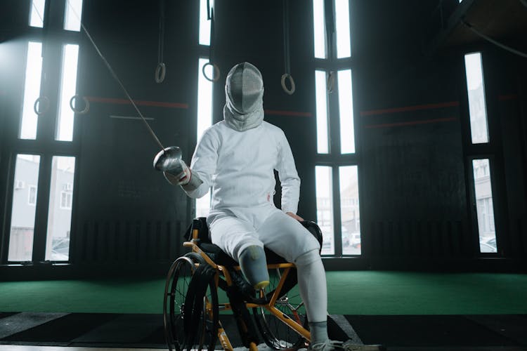 A Paralympic Athlete Wearing Fencing Equipment And Sitting On A Wheelchair