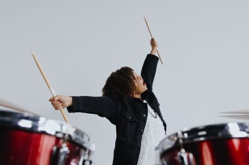 Free Young musician with curly hair joyfully plays drums, showcasing enthusiasm and talent. Stock Photo