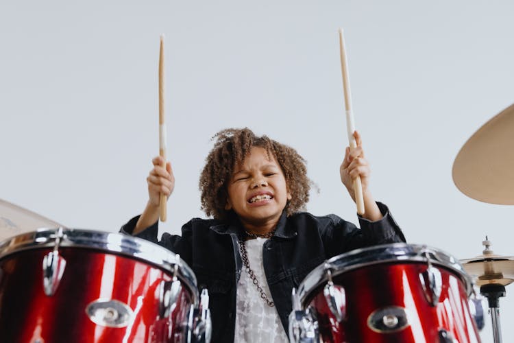 Photograph Of A Kid With Drumsticks Playing The Drums