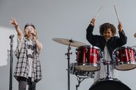 Photograph of a Kid Playing the Drums Beside a Child Singing