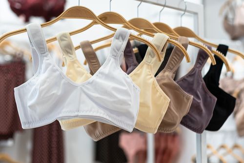Free Close-up of sports bras in various colors displayed on wooden hangers in a fashion store. Stock Photo