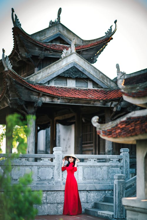 A Woman in Red Dress Standing Beside  Gray Concrete Building