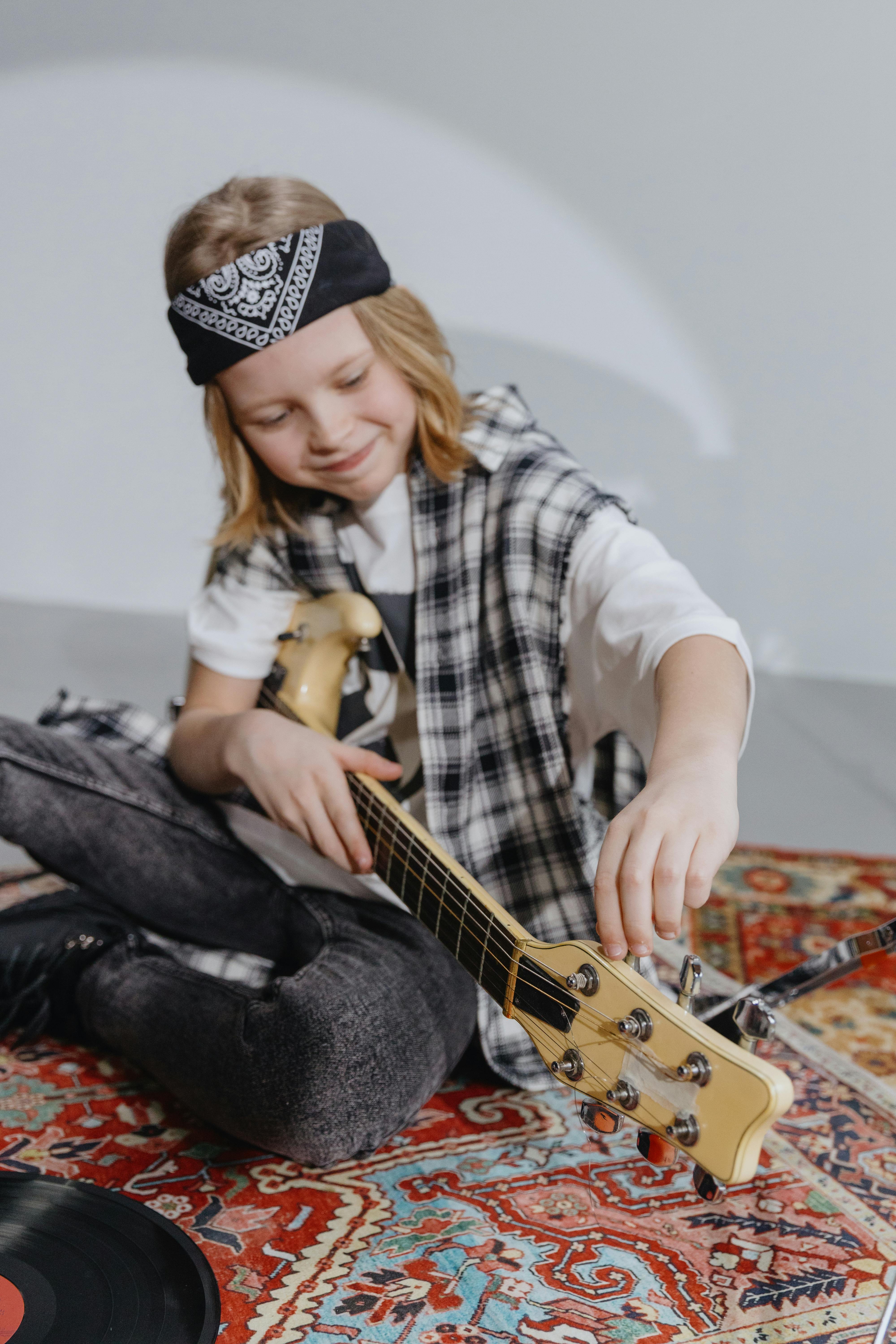 Kid tuning an electric guitar while sitting on a colorful rug, showcasing musical creativity.