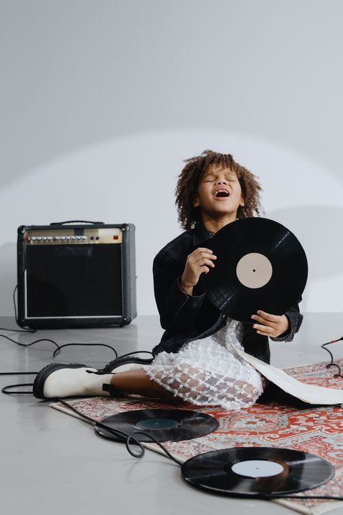 Free Girl joyfully singing while holding vinyl records and sitting near an amplifier. Stock Photo