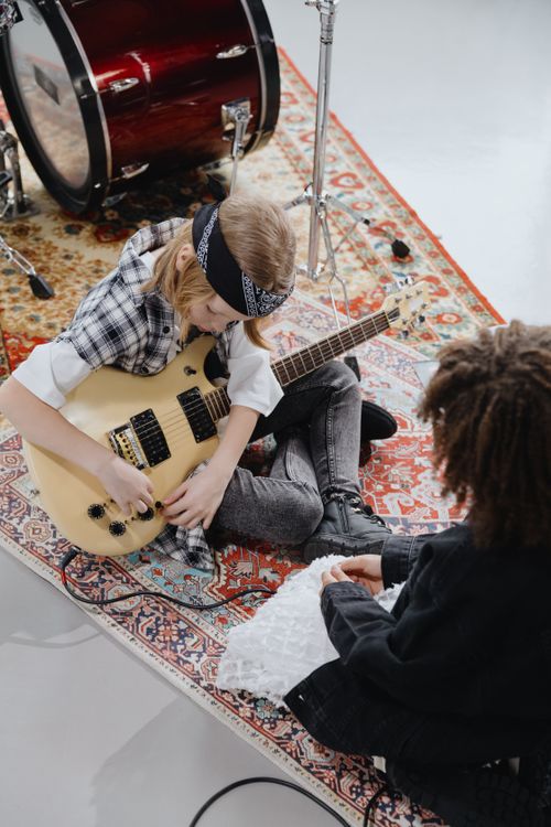Free Two children enjoying music with a guitar and drums on a decorative rug. Stock Photo