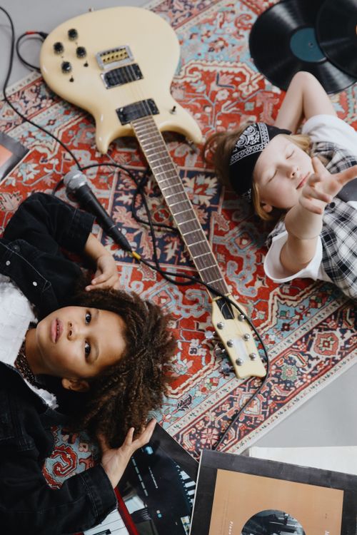 Free Two kids playing with electric guitar and vinyl records on a decorative rug, embracing rock band fun. Stock Photo