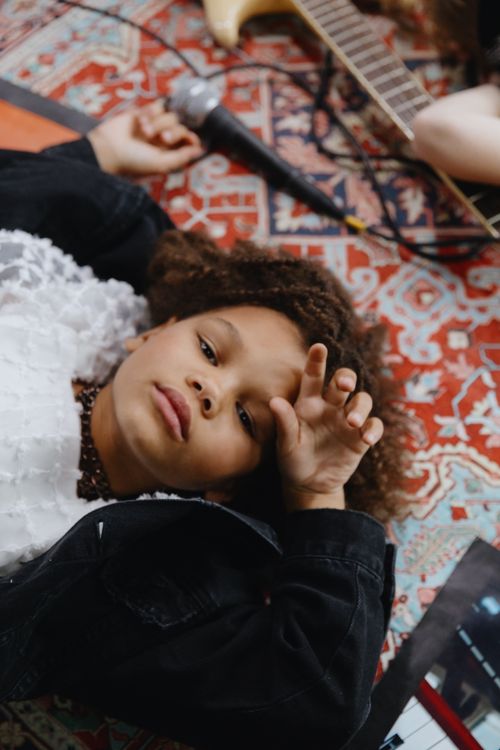 Free Charming child laying on a vibrant rug, holding a microphone amidst musical instruments. Stock Photo