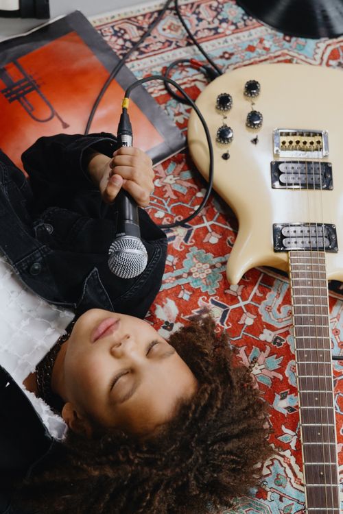 Free Child lying on a rug with a microphone and electric guitar, expressing musical creativity. Stock Photo