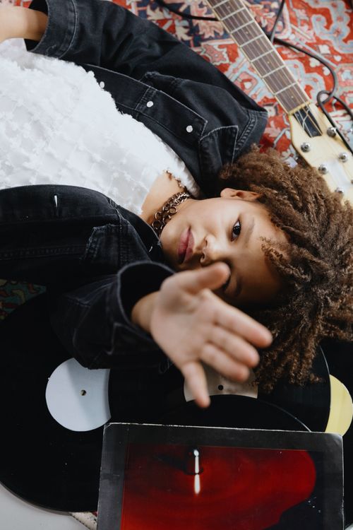 Free A child lying down with a guitar and vinyl records in an artistic composition indoors. Stock Photo