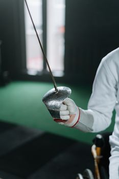 A detailed view of a fencer's hand holding a sabre indoors, highlighting sportsmanship.