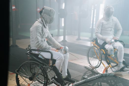 Two male wheelchair fencers practicing in a gym, focusing on training and skill development.