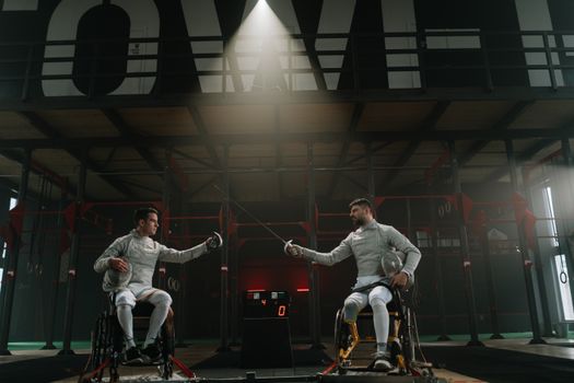 Two male wheelchair fencers in a competitive indoor match, showcasing adaptive sports.