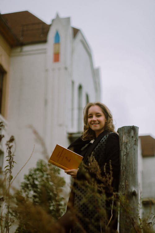 Photo of a Woman Holding a Book while Smiling at the Camera