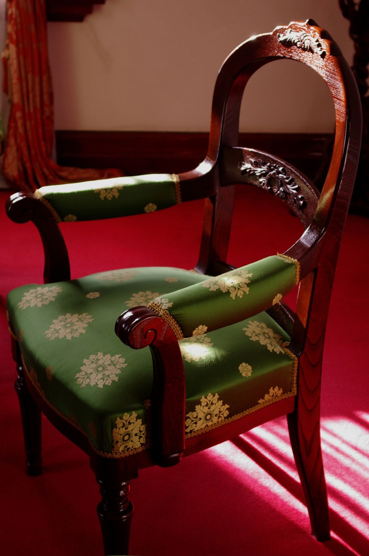 Dark carved armchair with green and gold damask upholstery in raking light