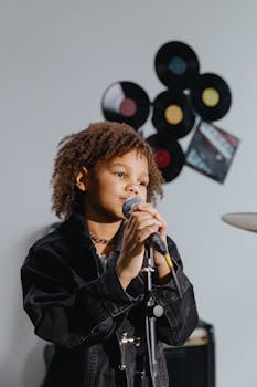 Charming young girl with afro hair sings passionately in a music-themed studio setting.