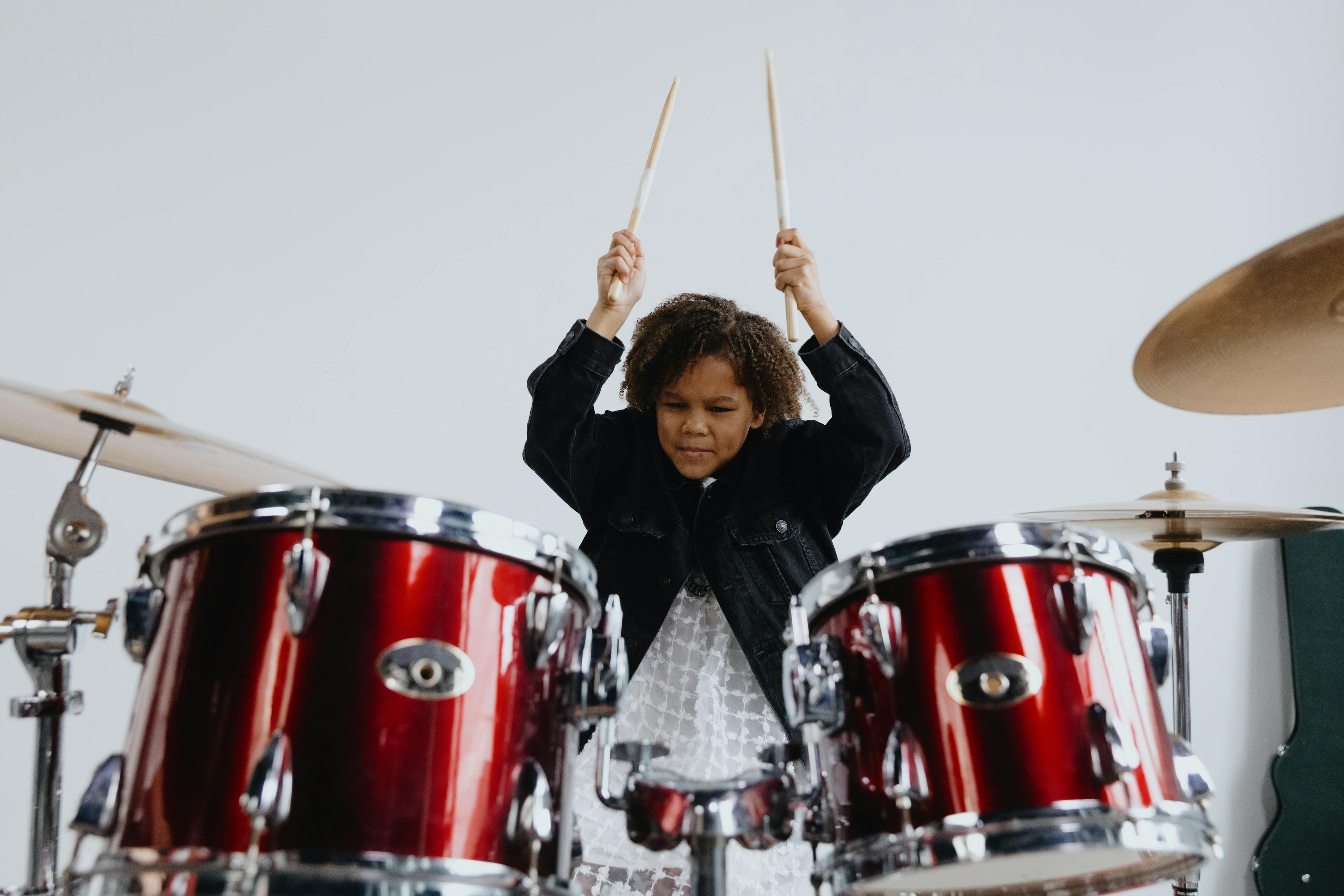 Close-up of a girl energetically playing a drum set indoors.