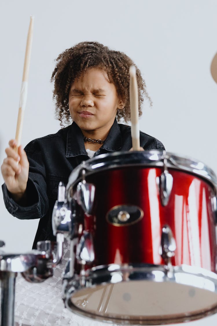 Photo Of A Child With Curly Hair Playing The Drums While Her Eyes Are Closed