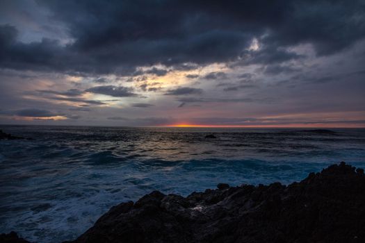 A captivating ocean sunset scene with dramatic clouds and waves crashing on rocky shores.