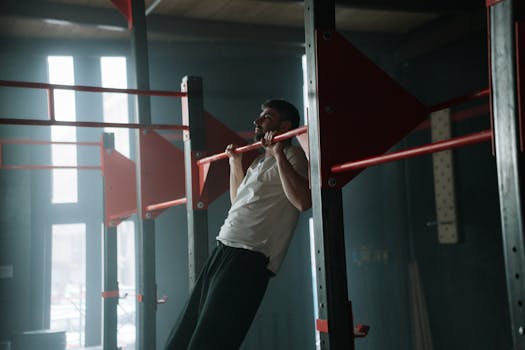 Adult man doing pull-ups in a dimly lit indoor gym, focused on upper body training.