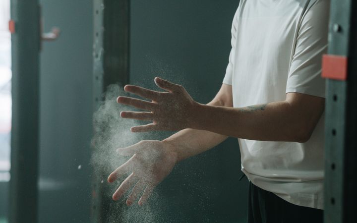 Man in gym applying chalk to hands before workout. Focused preparation for intense physical activity.