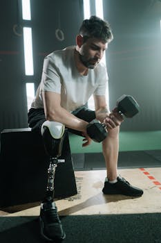 Determined athlete with prosthetic leg lifting dumbbell indoors, showcasing strength and resilience.
