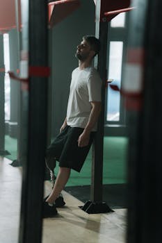 Adaptive athlete with a prosthetic leg leaning against gym equipment indoors.
