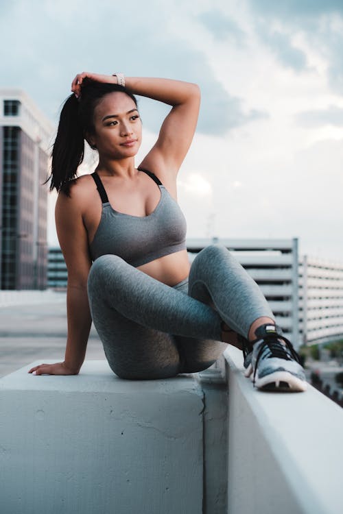 A Woman in Gray Leggings and Sports Bra Sitting with Her Hand on Her Head · Free  Stock Photo