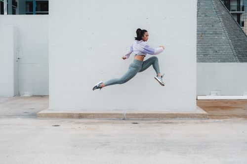 Free Asian woman in activewear jumping energetically against a minimalistic urban backdrop in Orlando. Stock Photo
