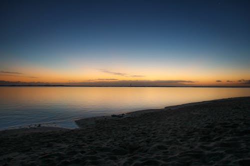 Body of Water Near Beige Sand Under Blue and White Sky at Sunset