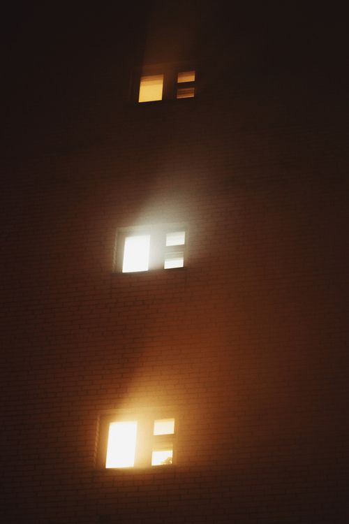Free Moody shot of illuminated windows in a foggy building exterior at night. Stock Photo