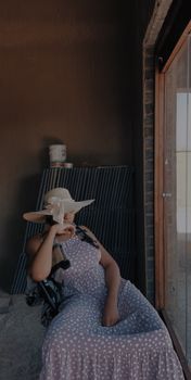 Woman in a polka dot dress and hat sitting indoors by a window with natural light.