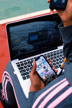 Person multitasking with smartphone and laptop outdoors, showcasing technology in everyday life.