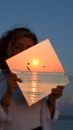 Photo manipulation of woman holding image of sunset over sea