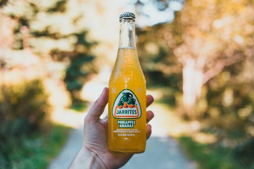 Free Hand holding a bottle of Jarritos pineapple soda outdoors in a sunny setting. Stock Photo