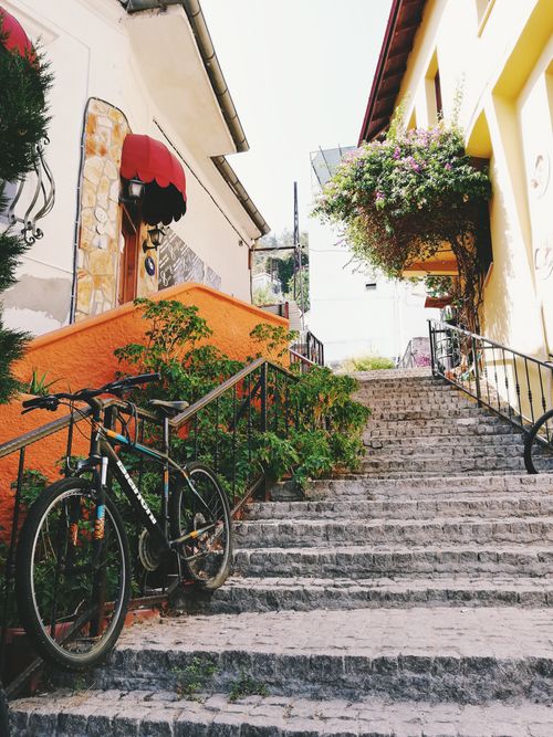 Free Picturesque city alley with bicycles, vibrant flowers, and stone stairs in sunlight. Stock Photo