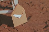 Open envelope with flowers resting on sandy beach next to a chair.