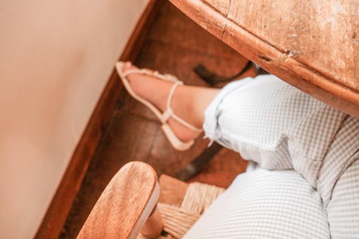 Elegant pastel checkered pants and sandal under wooden table, top view.