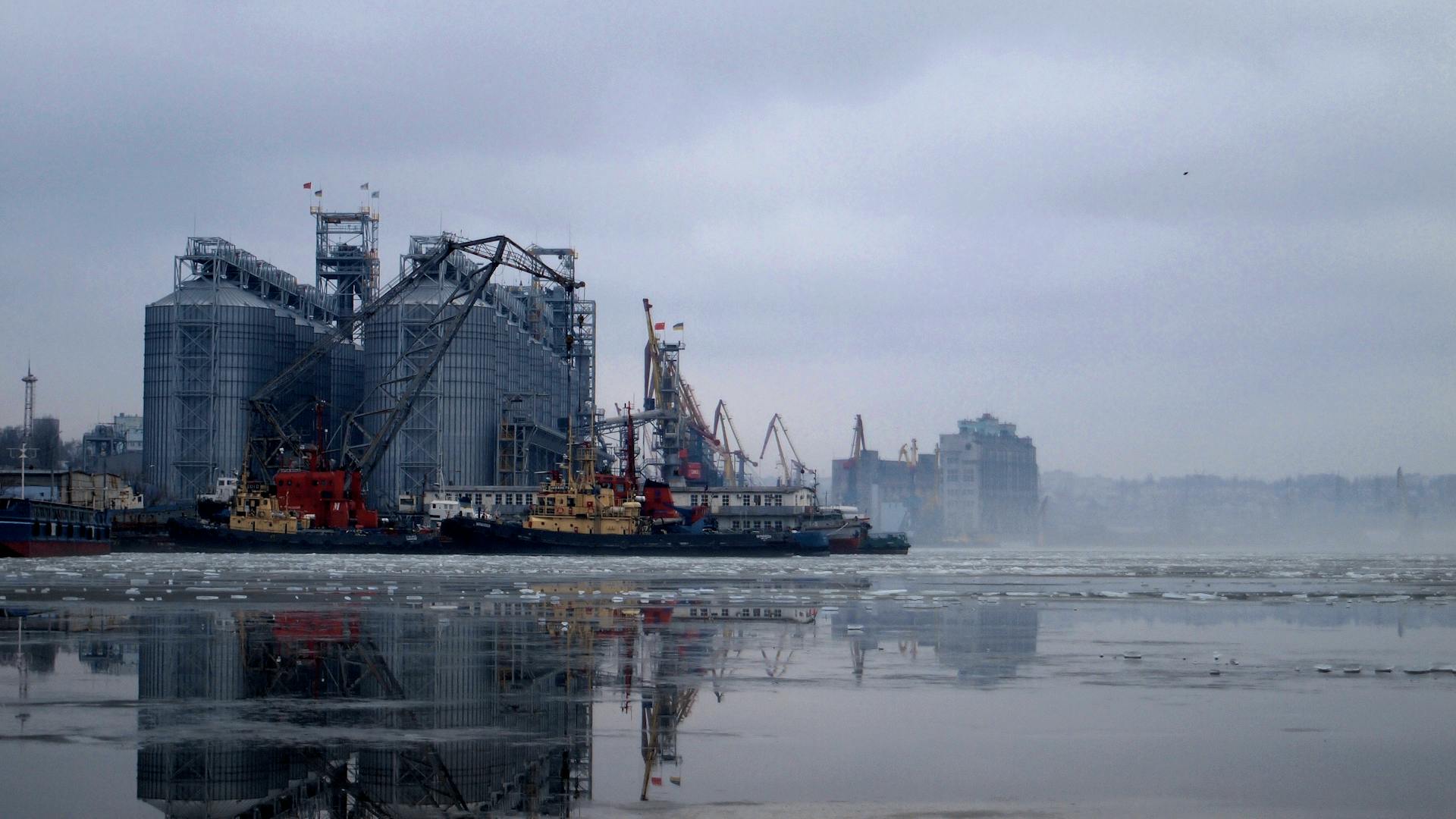A wide shot of an industrial port facility with grain silos and cranes on a foggy winter day.