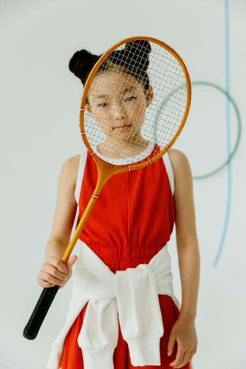 Free Portrait of an Asian girl in a red sports outfit holding a badminton racket indoors. Stock Photo