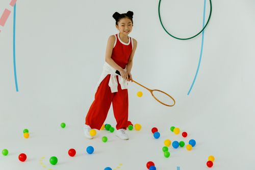 Free Smiling young girl in red sportswear playing with colorful balls indoors, enjoying her time. Stock Photo