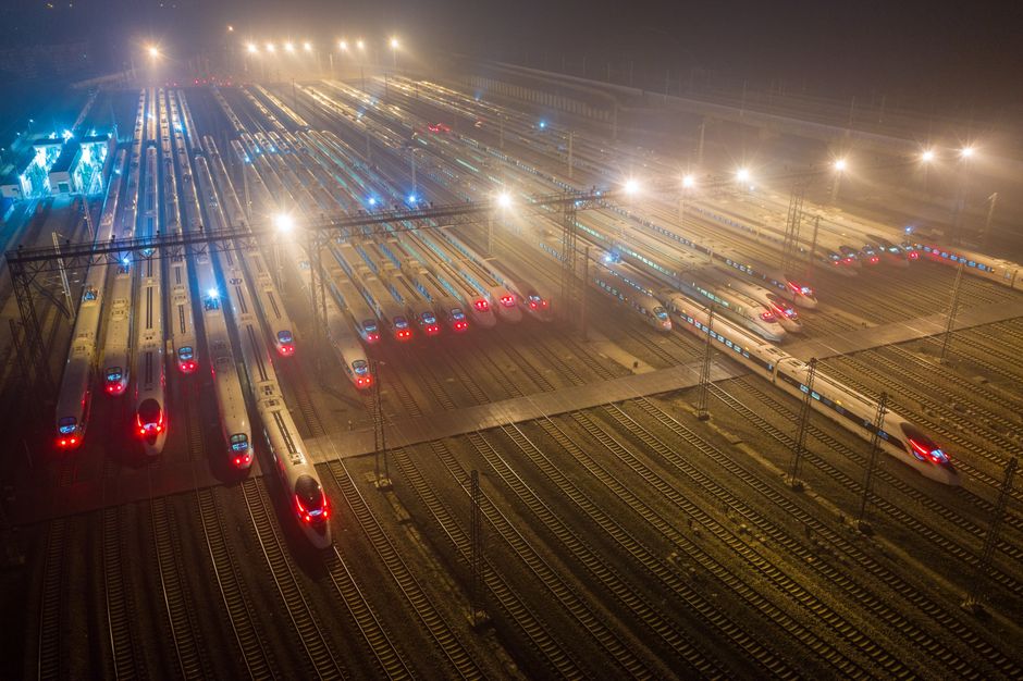 Dramatic aerial night view of a bustling train station with numerous high-speed trains lined up.