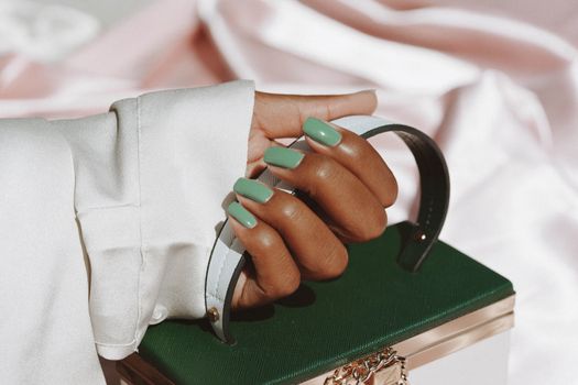 Close-up of a woman's hand with green nails holding a stylish handbag, showcasing fashion and elegance.