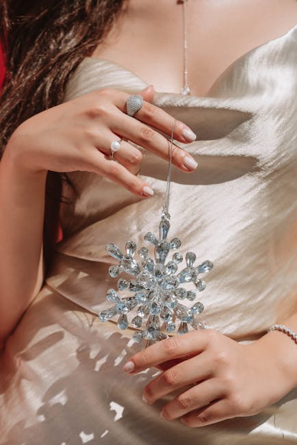 A woman in a satin dress holds a crystal snowflake ornament, highlighting elegance.