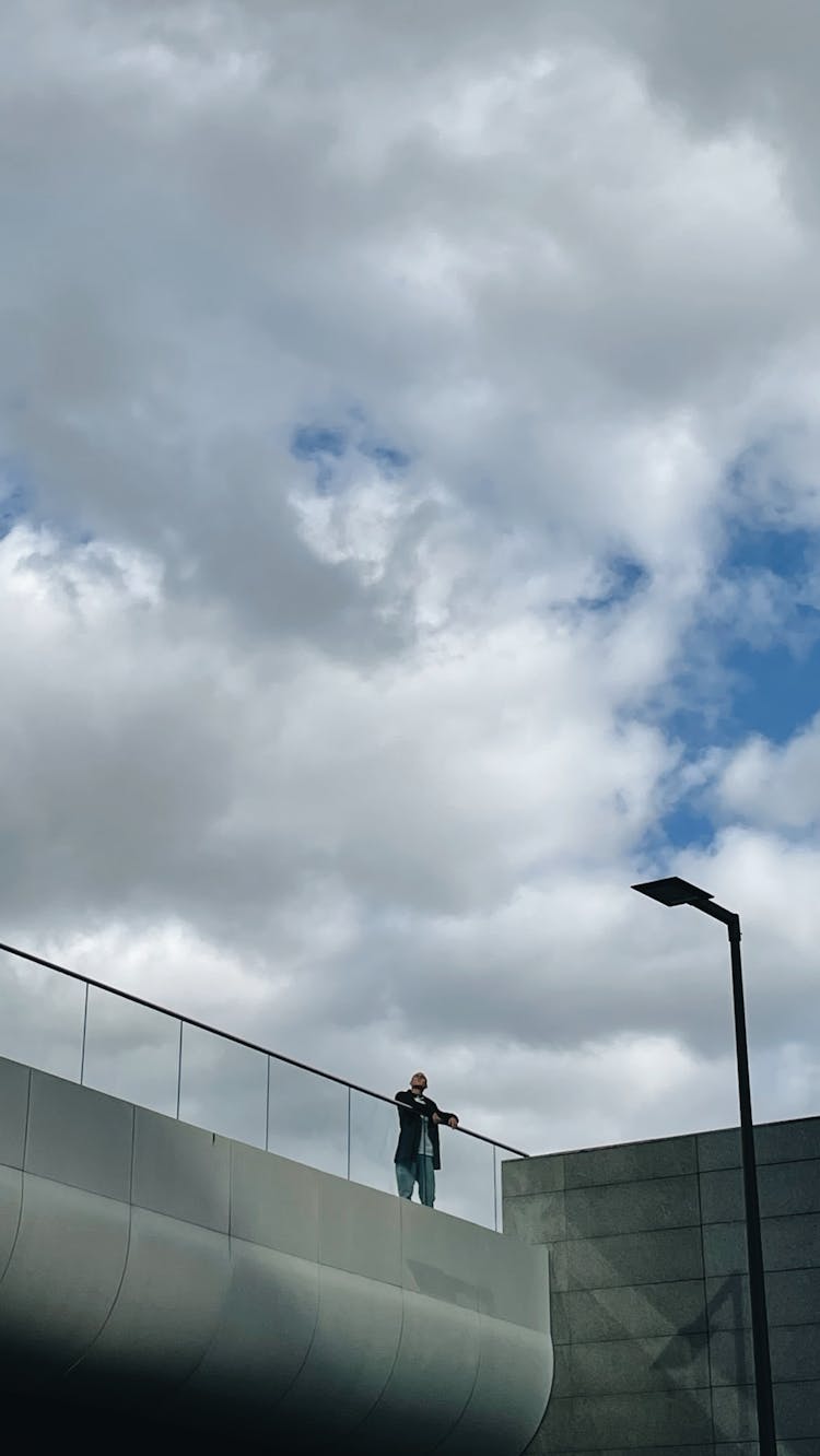 Man Standing By Barrier Under Clouds