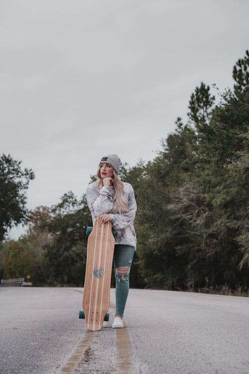 Free Woman Standing on the Road while Holding a Longboard Stock Photo