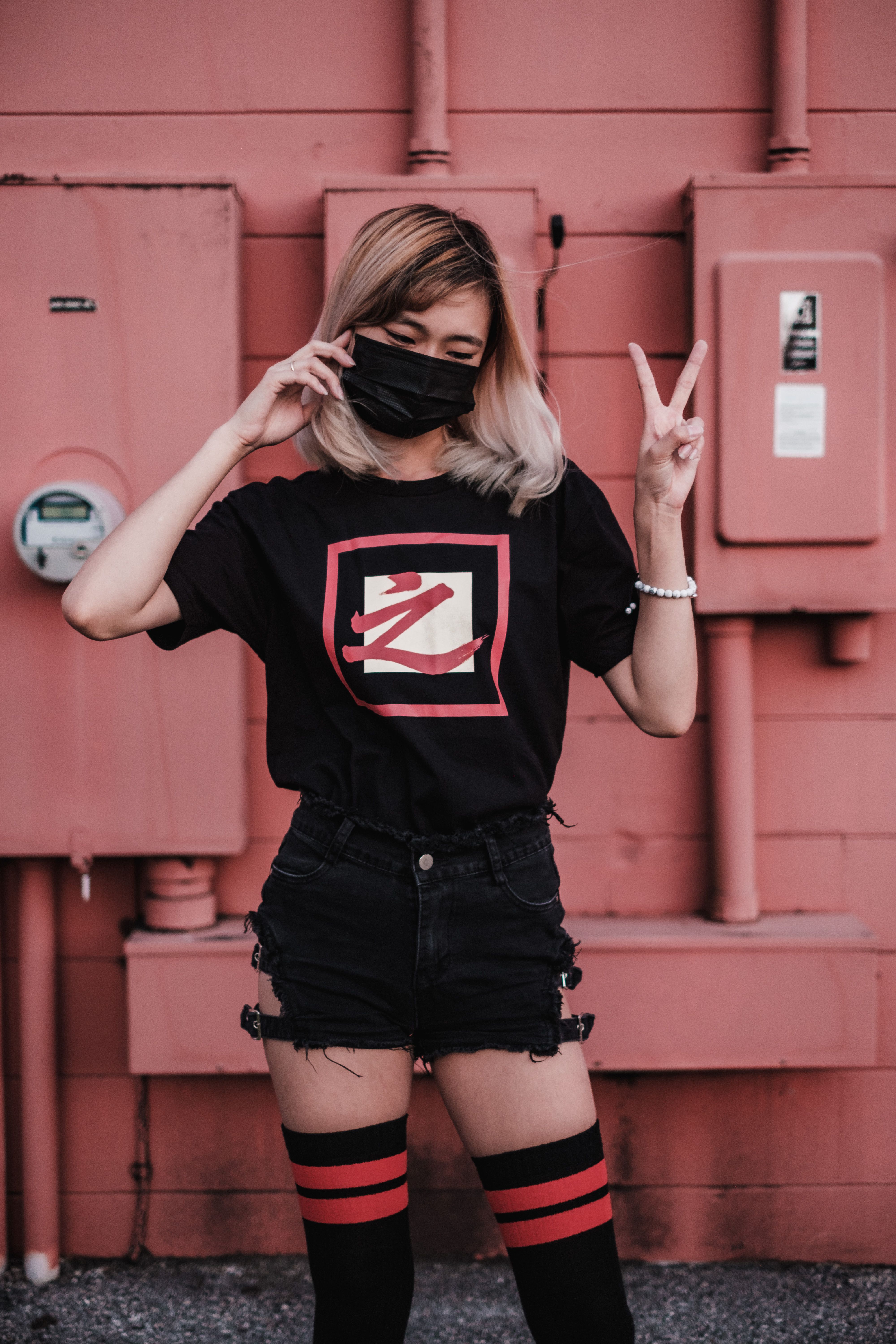 An Asian woman in a stylish black outfit strikes a peace sign pose outdoors.
