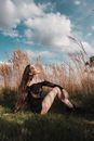 Woman in Black Dress Sitting on Green Grass Field Under Blue and White Cloudy Sky during