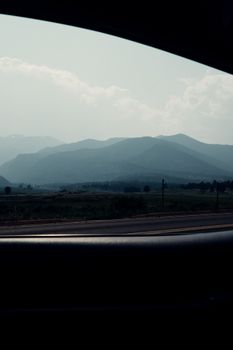 Mountain range view framed by a car window during daylight, evoking a sense of travel and adventure.