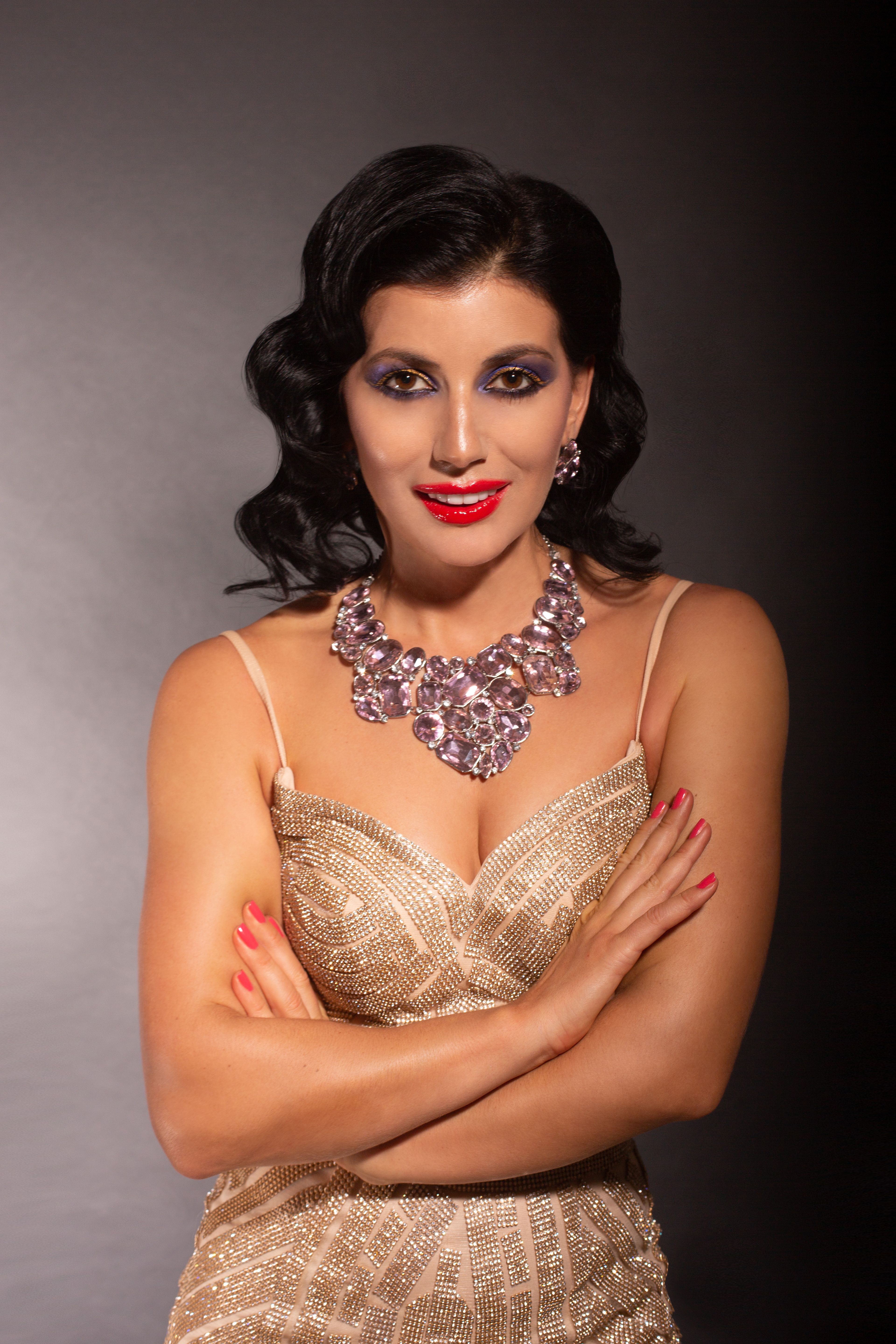 Portrait of a woman with bold makeup and statement necklace in a studio setting.